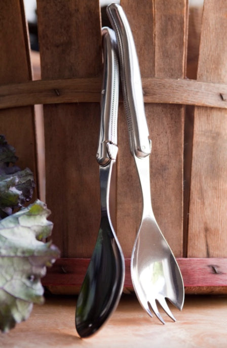 Laguiole Platine Salad Serving Set leaning beside a barrel